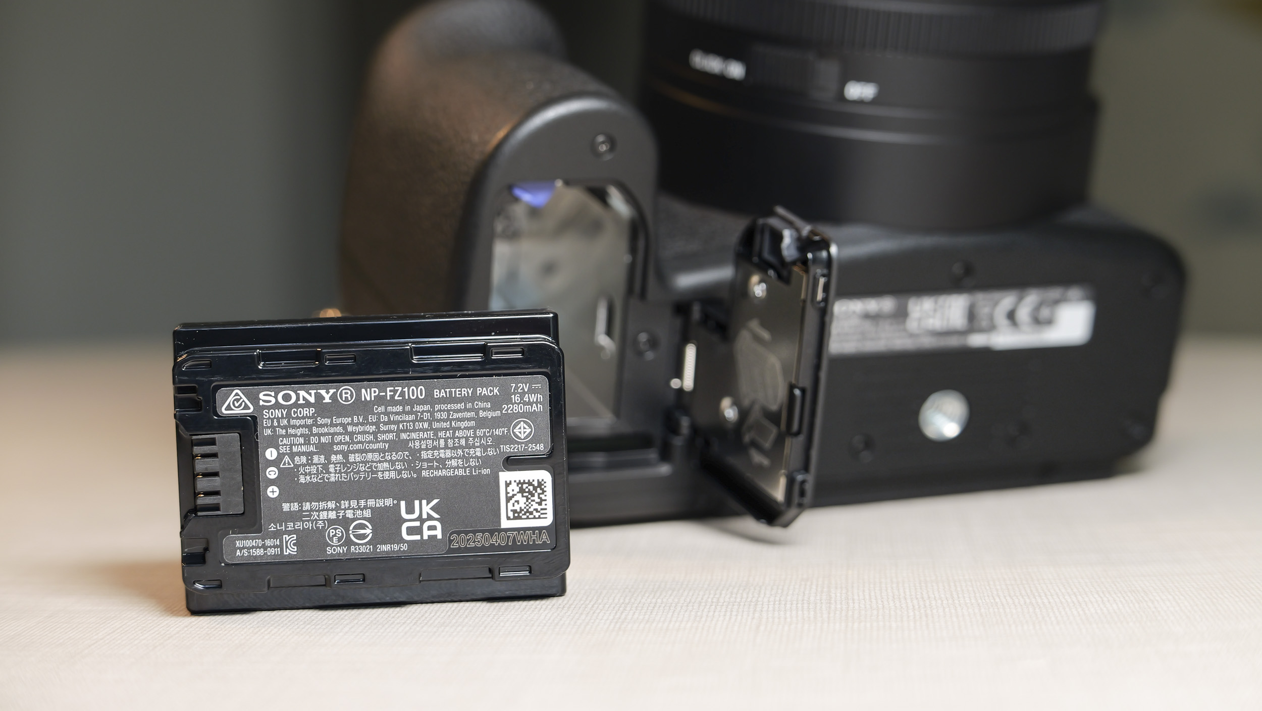 Closeup of the Sony RX10 V bridge camera's battery door, and the battery has been removed and placed on the table in front of the camera