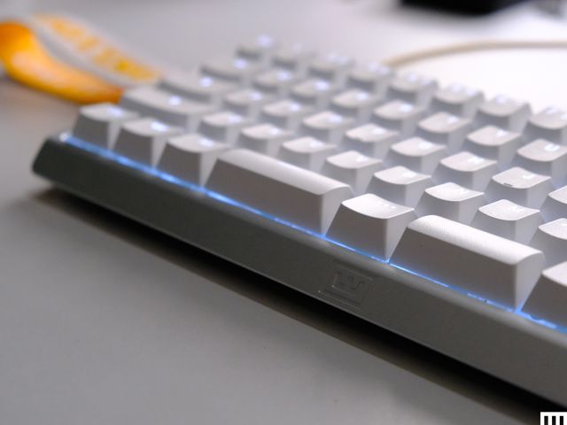 Closeup of the front edge of a white computer keyboard with illuminated keys